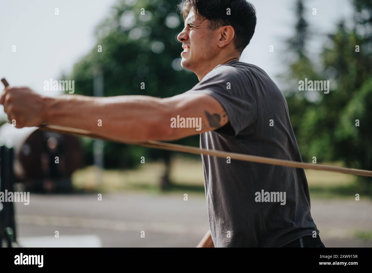Ein fokussierter Mann, der im Outdoor-Park ein Calisthenics-Workout mit Widerstandsband durchführt Stockfoto