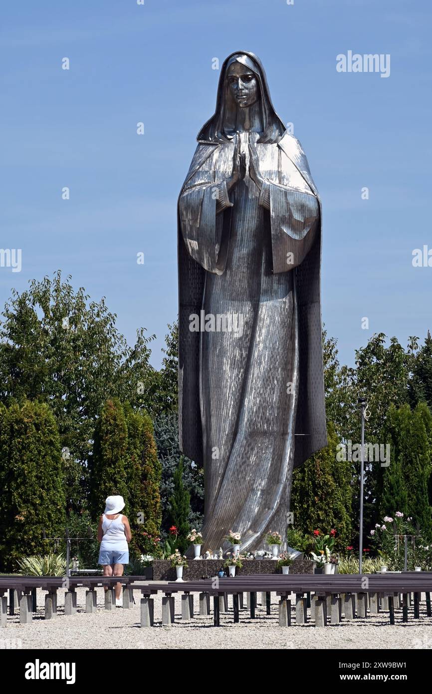 Große Edelstahlstatue der Jungfrau Maria am Vodica-Mariakert-Schrein in Hercegszántó mit einsamer Frau, die im Sommer aus einem Winkel betet Stockfoto