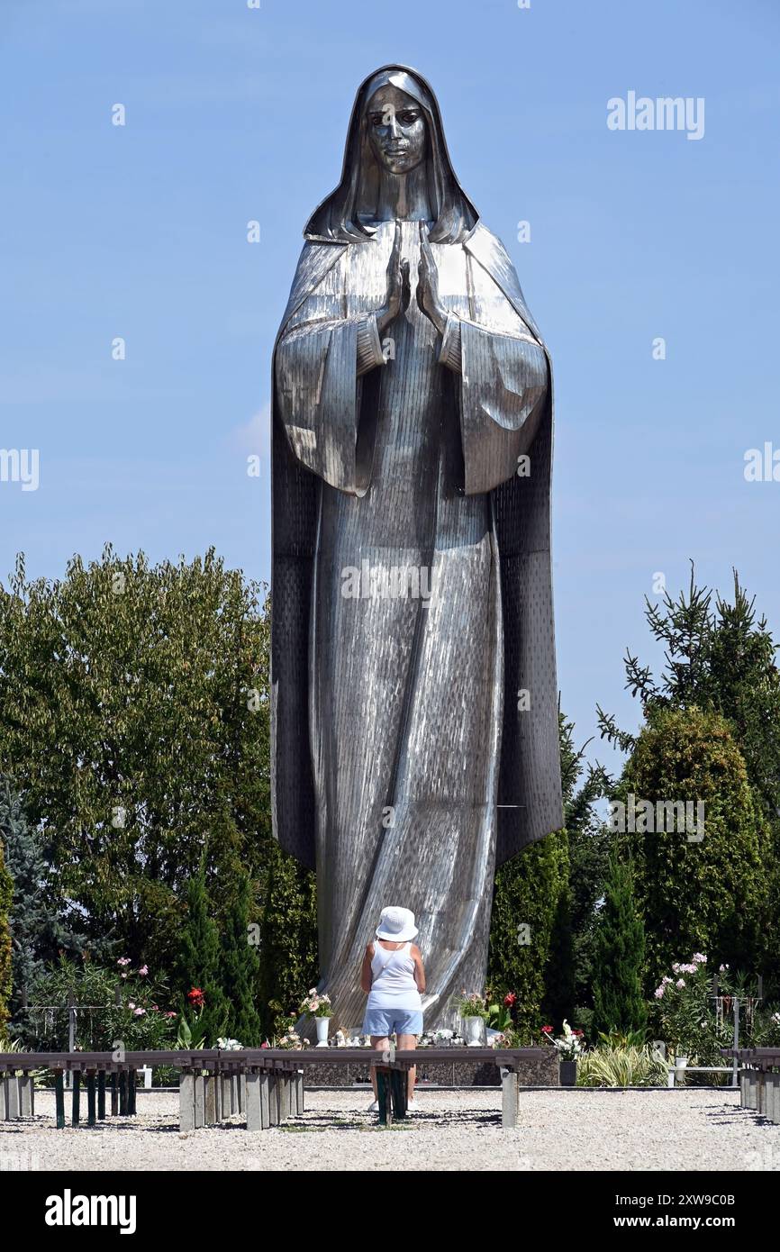 Große Edelstahlstatue der Jungfrau Maria am Vodica-Mariakert-Schrein in Hercegszántó mit einsamer Frau, die im Sommer von vorne betet Stockfoto