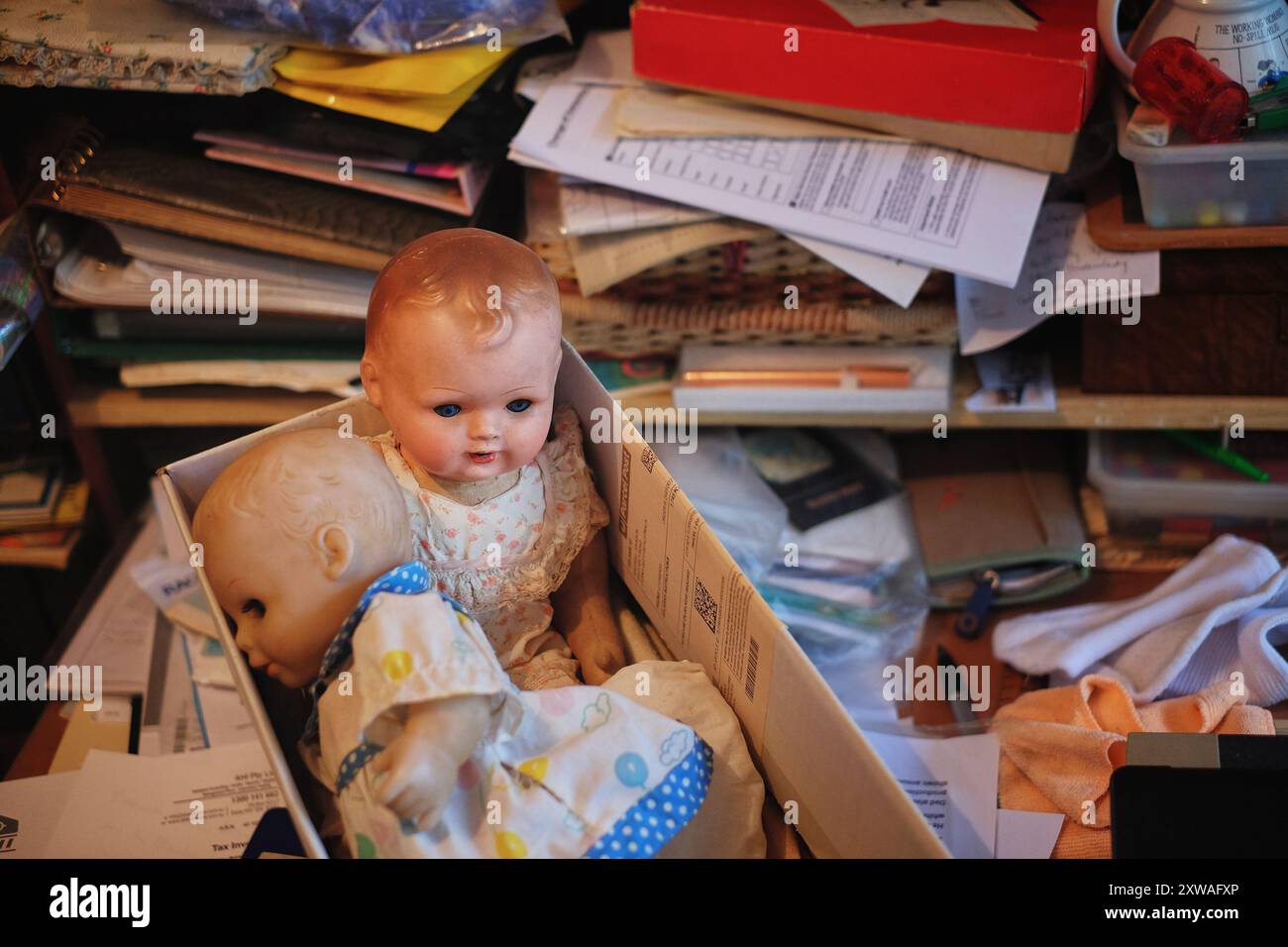 Puppen und Papierkram auf einem überladenen Schreibtisch, ältere Eltern, die im eigenen Haus leben, Fotoalben, Nähkorb, Notizen und Lebensphären. Stockfoto