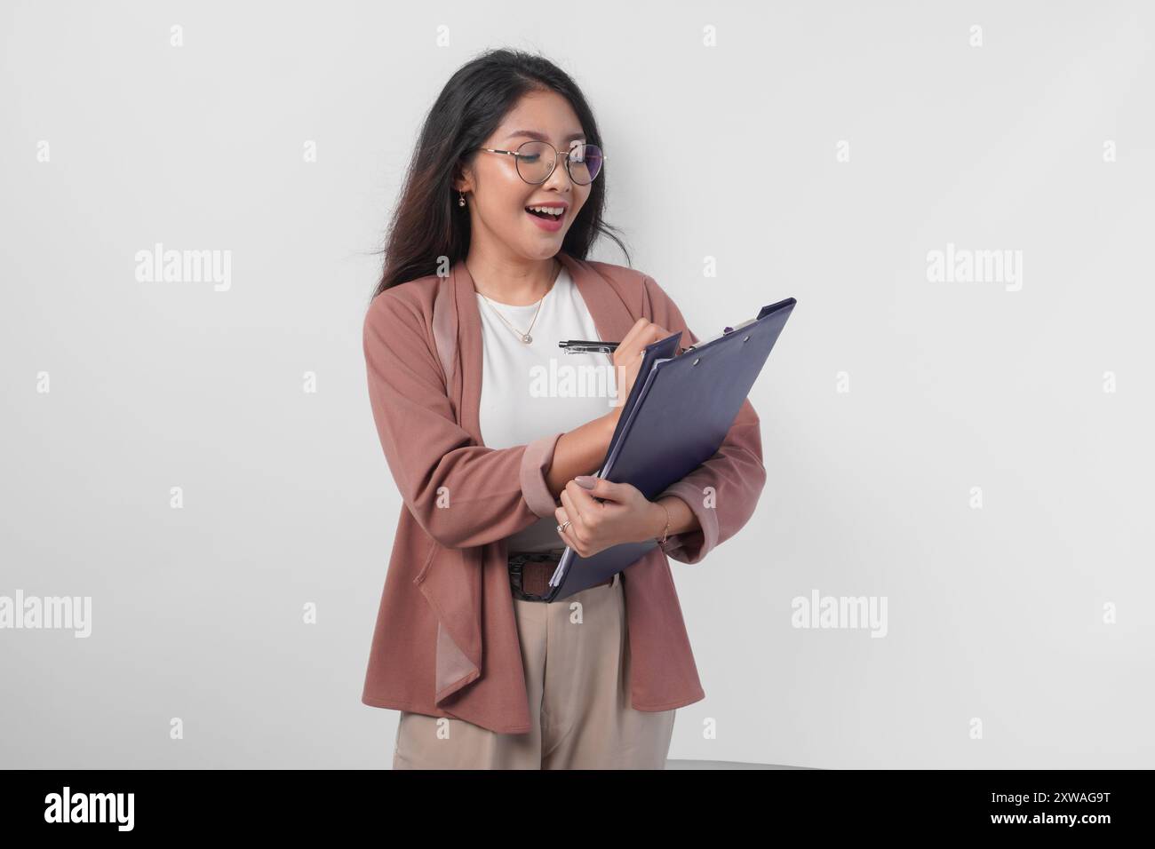 Junge asiatische Geschäftsfrau in Brille, die ein Dokument und einen Stift hält, um Bericht zu schreiben, isoliert durch weißen Hintergrund. Stockfoto