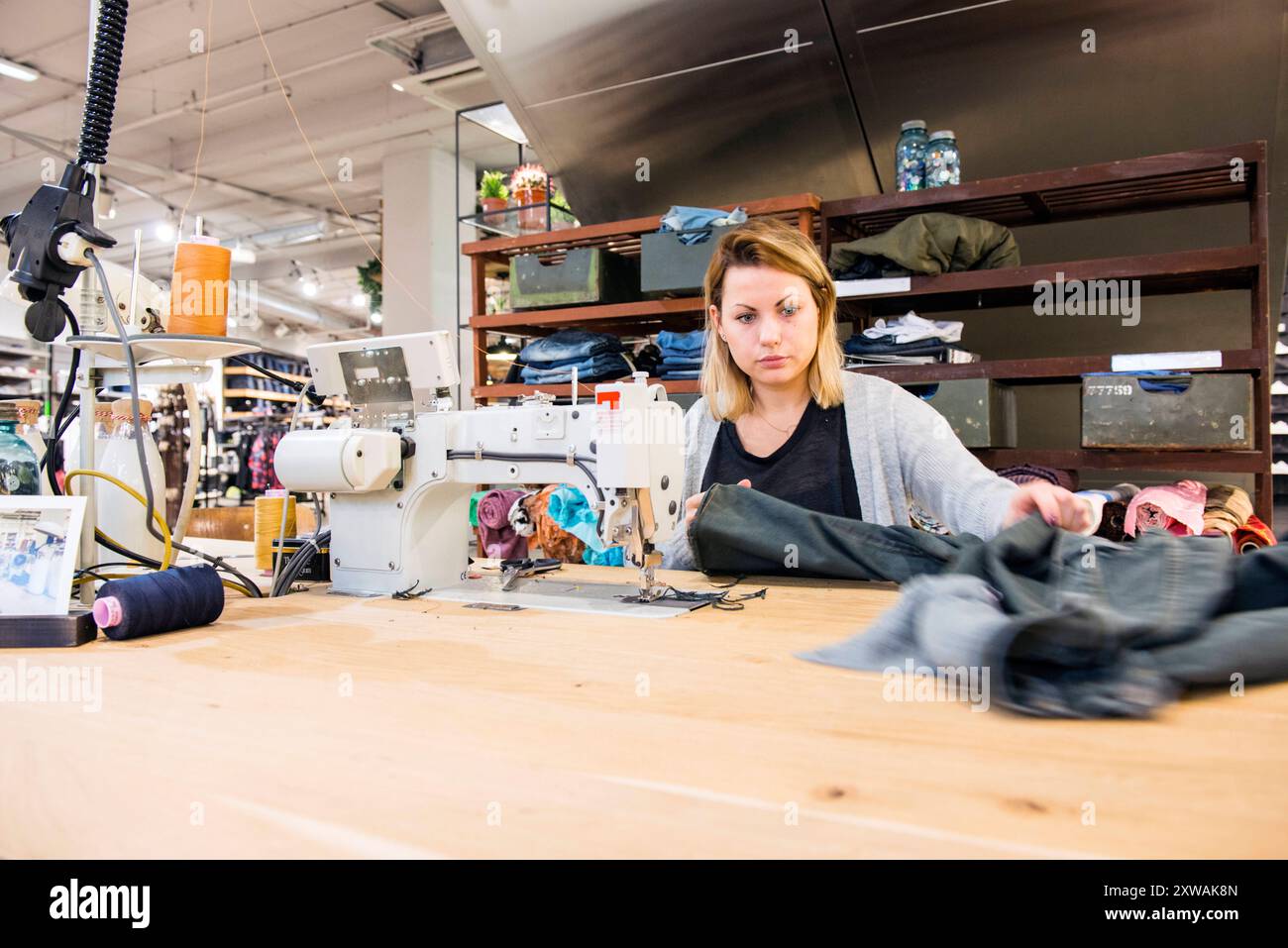 Needlewoman Hard at Work Jamie, ein Needlewman bei MenWork, der eine neue Jeans für einen Kunden verkürzt. Tilburg, Niederlande. MRYES Tilburg MenWork Fashionstore, Pieter VR Noord-Brabant Nederland Copyright: XGuidoxKoppesxPhotox Stockfoto