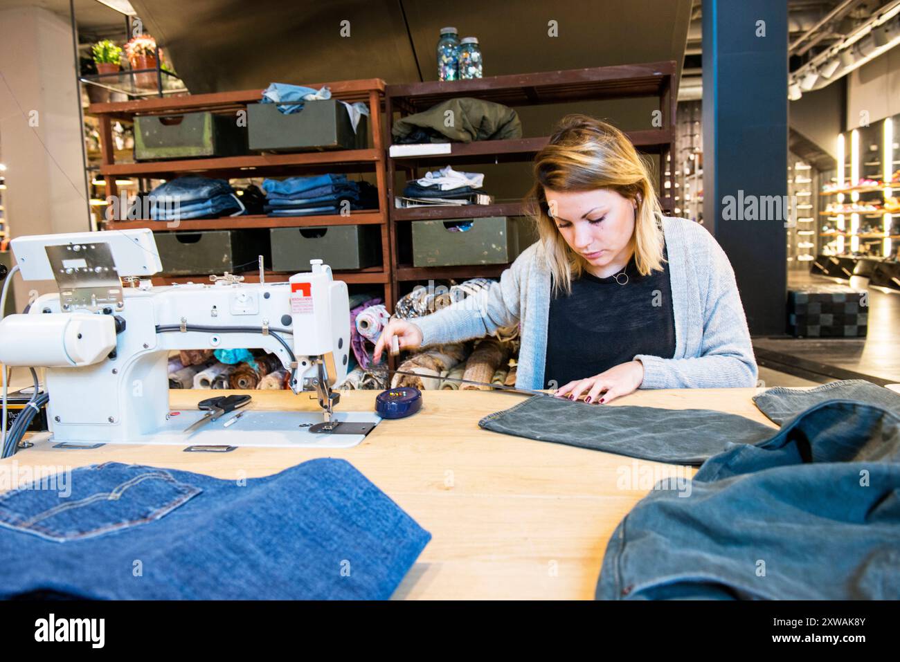 Needlewoman Hard at Work Jamie, ein Needlewman bei MenWork, der eine neue Jeans für einen Kunden verkürzt. Tilburg, Niederlande. MRYES Tilburg MenWork Fashionstore, Pieter VR Noord-Brabant Nederland Copyright: XGuidoxKoppesxPhotox Stockfoto