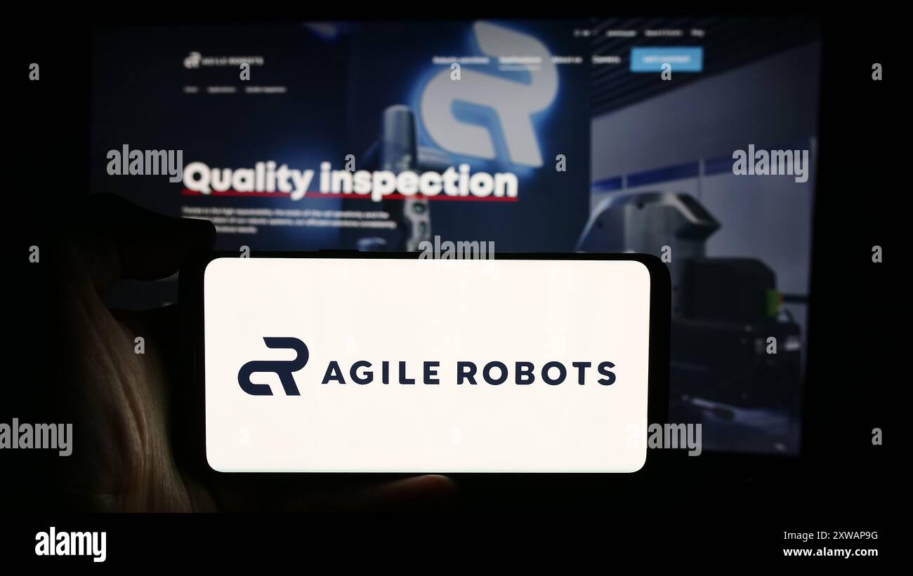 Person, die ein Mobiltelefon mit dem Logo des deutschen Roboterunternehmens Agile Robots SE vor der Business-Website hält. Schwerpunkt auf dem Display des Telefons. Stockfoto