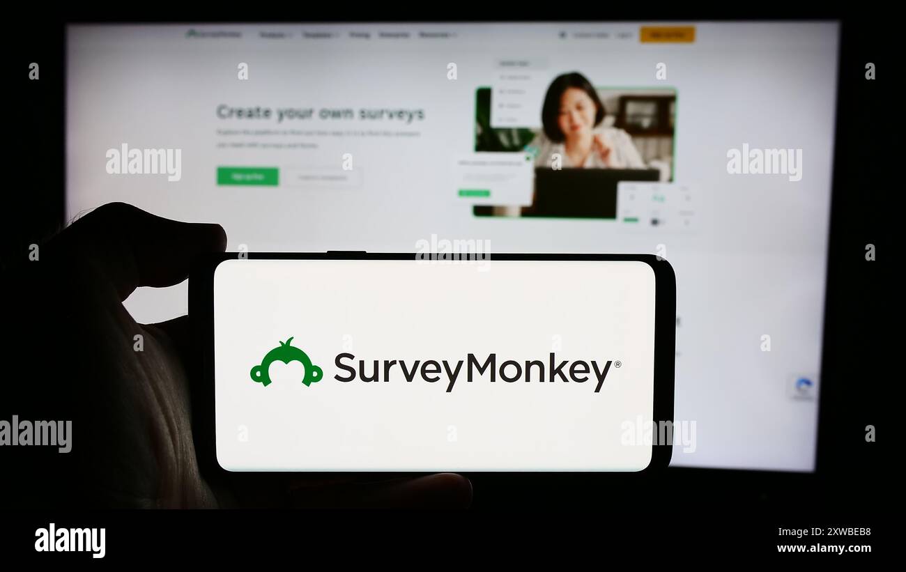 Person, die ein Mobiltelefon mit dem Logo des US-amerikanischen Softwareunternehmens SurveyMonkey Inc. Vor der Webseite des Unternehmens hält. Schwerpunkt auf dem Display des Telefons. Stockfoto