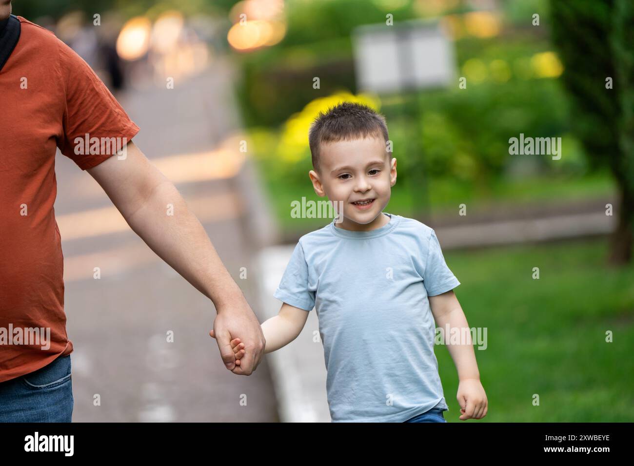 Ein glücklicher dreieinhalb-jähriger Sohn geht Hand in Hand mit seinem Vater an einem sonnigen Sommertag im Park. Familienspaß und Freizeit. Sommer. Close-u Stockfoto