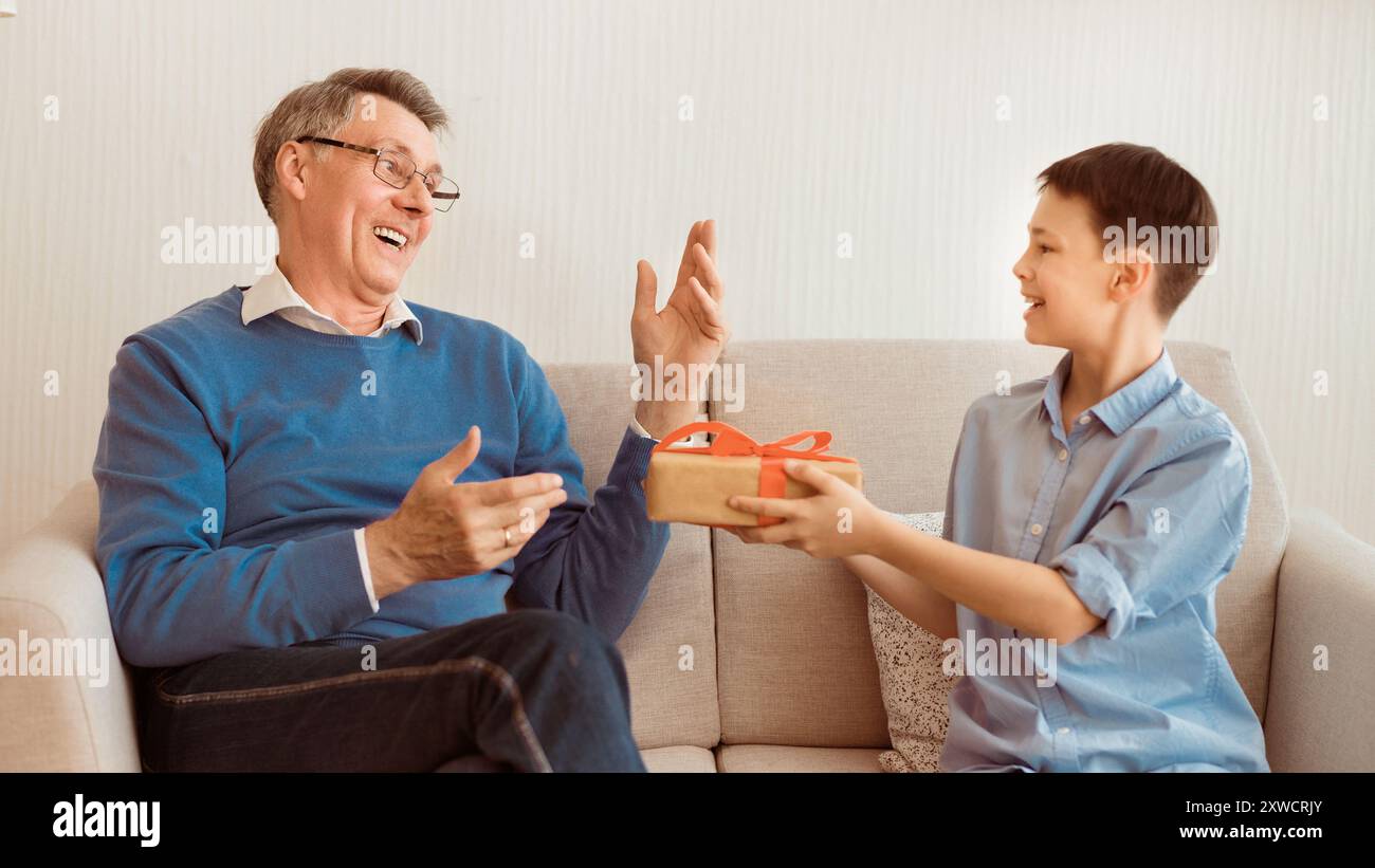 Enkel gratulieren Großvater, verpackte Geschenk Sitzen auf einem Sofa, Panorama Stockfoto