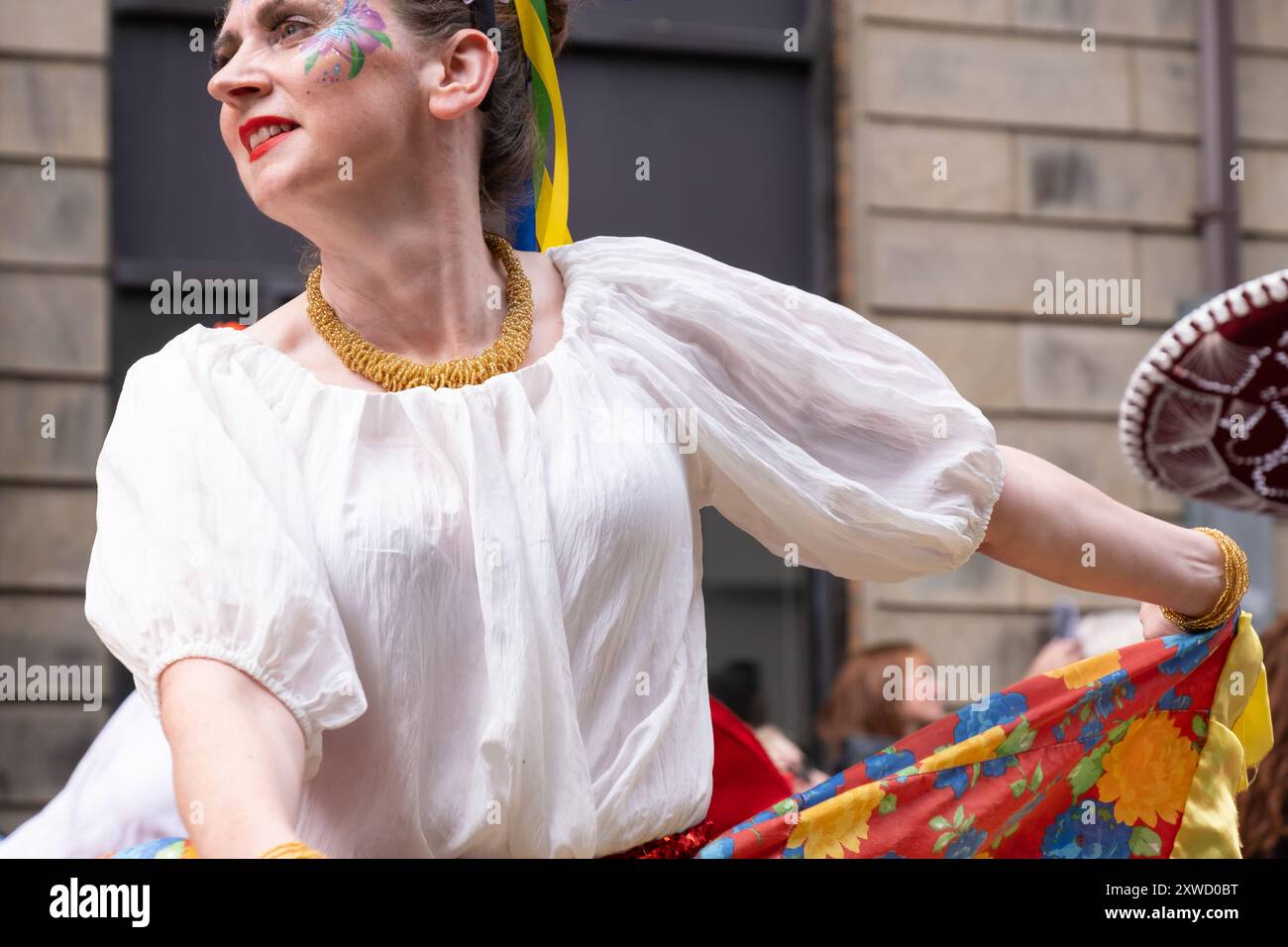 Frau in farbenfrohem Kleid mit gemalter Dekoration auf Gesichts tanzen bei der jährlichen Karnevalsparade in Belfast Mela im Stadtzentrum. Belfast, Großbritannien - 17. August 2024. Stockfoto