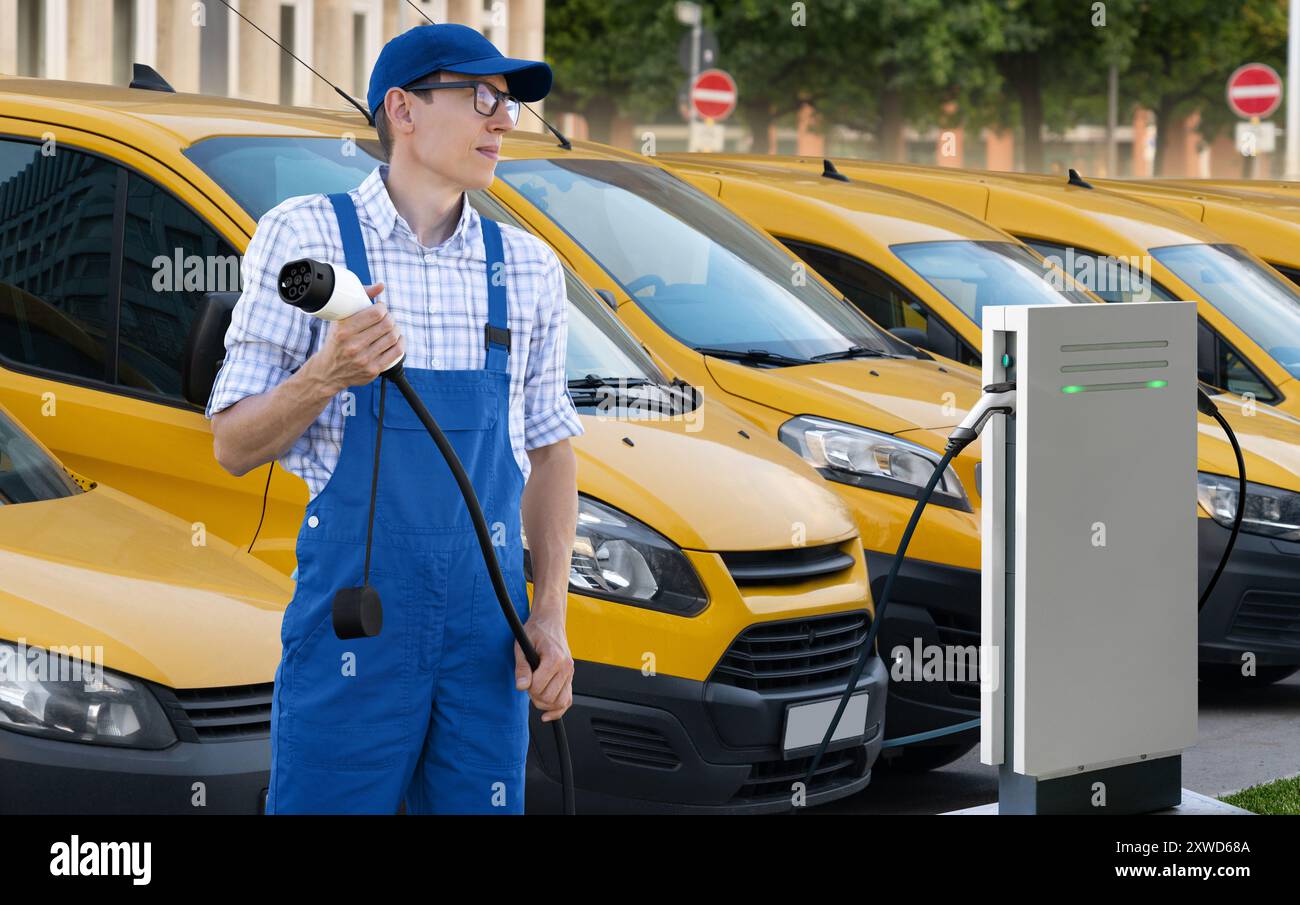 Mann in Uniform hält den Ladestecker für Elektrofahrzeuge. Elektrische Lieferwagen im Hintergrund. Stockfoto