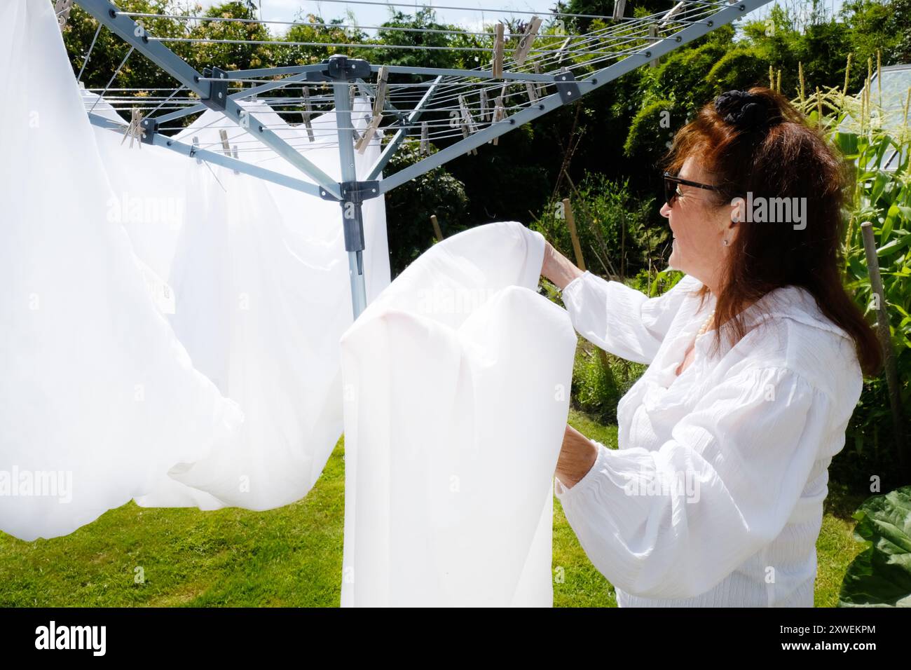 Reife Frau, die weiße Bettlaken an einer rotierenden Wäscheleine hängt - John Gollop Stockfoto