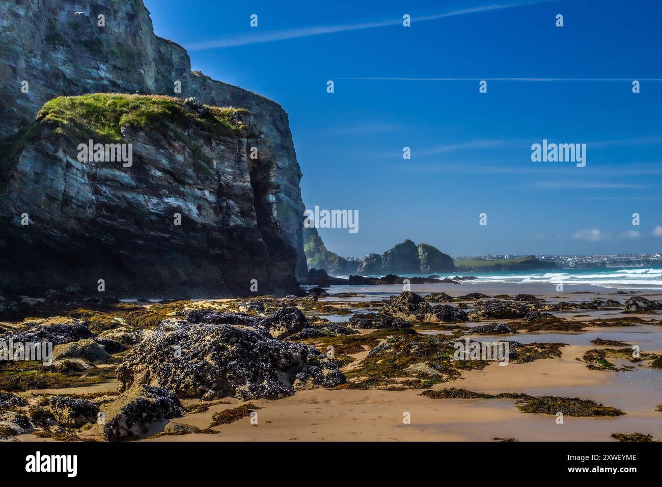 Herrliche Strandszene Watergate Bay, Cornwall. Ein heißer Tag in der Hochsommerhitze. Wellen im Hintergrund, Felsen im Vordergrund. Blauer Himmel, tolles Licht! Stockfoto