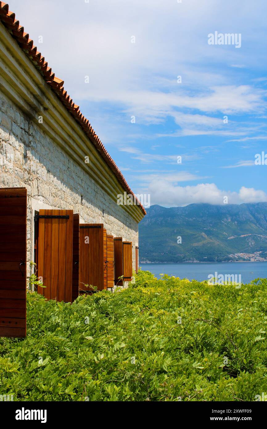 Europäisches Backsteinhaus mit grünem Weinberg auf dem Hof in Budva. Die Landschaft der Lagune und der Berge Montenegros öffnet sich hinten Stockfoto