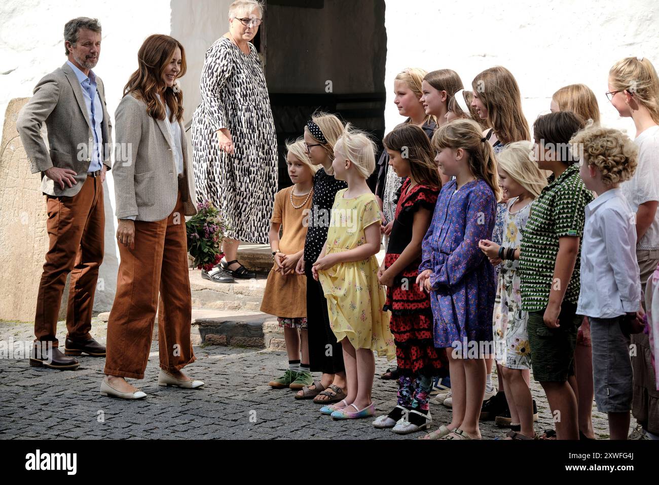 König Frederik X und Königin Maria besuchen am Montag, 19. August 2024 die Regionalgemeinde Bornholm. Das Königspaar kommt in der OEsterlars Church in Gudhjem an und wird vom Vorsitzenden des gemeinderates Erling Aabye Dam und der Pfarrer Tina Ravnsbjerg Damholt empfangen, nach der der Kinderchor der Kirche ein Lied aufführt. Die OEsterlars Kirche ist die größte und älteste der vier runden Kirchen Bornholms. Während des Besuchs nimmt das königliche Paar an einer Führung durch die Kirche Teil und wird unter anderem über die Fresken der Kirche informiert und die Gelegenheit erhalten, die Holzfassade der Kirche zu besichtigen. (Ph Stockfoto