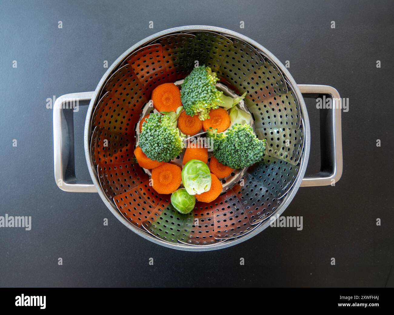 Zusammenklappbarer Dampfkorb in einem Topf mit Brokkoli, Karotten und Rosenkohl. Durch das Dampfgaren bleiben die wichtigen Nährstoffe erhalten, der Geschmack und die h erhalten Stockfoto