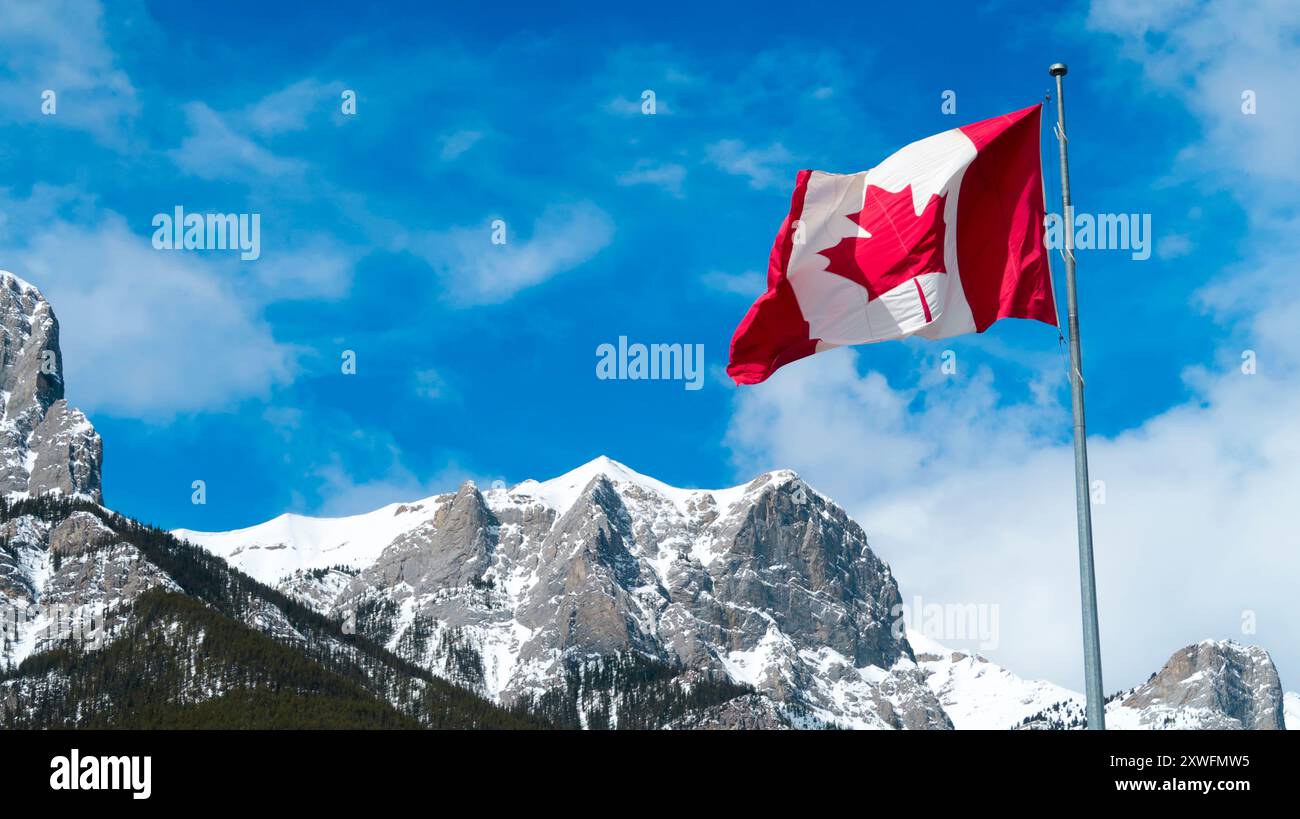 Die kanadische Flagge fliegt am Pfosten gegen den blauen Himmel und die Berge Stockfoto