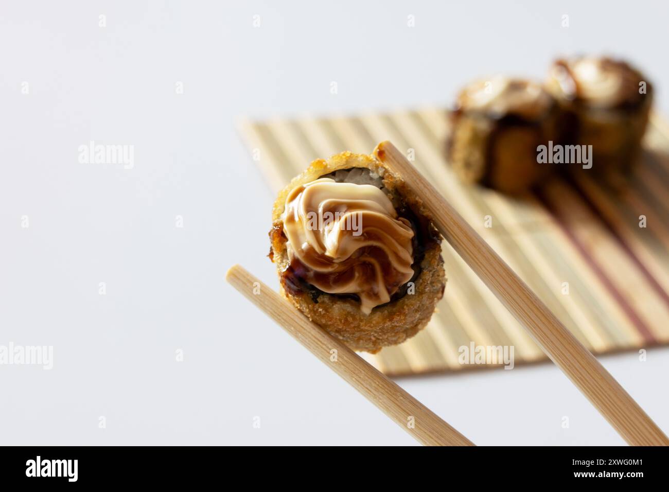 Zwei Essstäbchen, die ein warmes Brötchen mit Frischkäse und Tara-Sauce auf einem Hintergrund halten, während andere heiße Brötchen außer Fokus stehen. Stockfoto