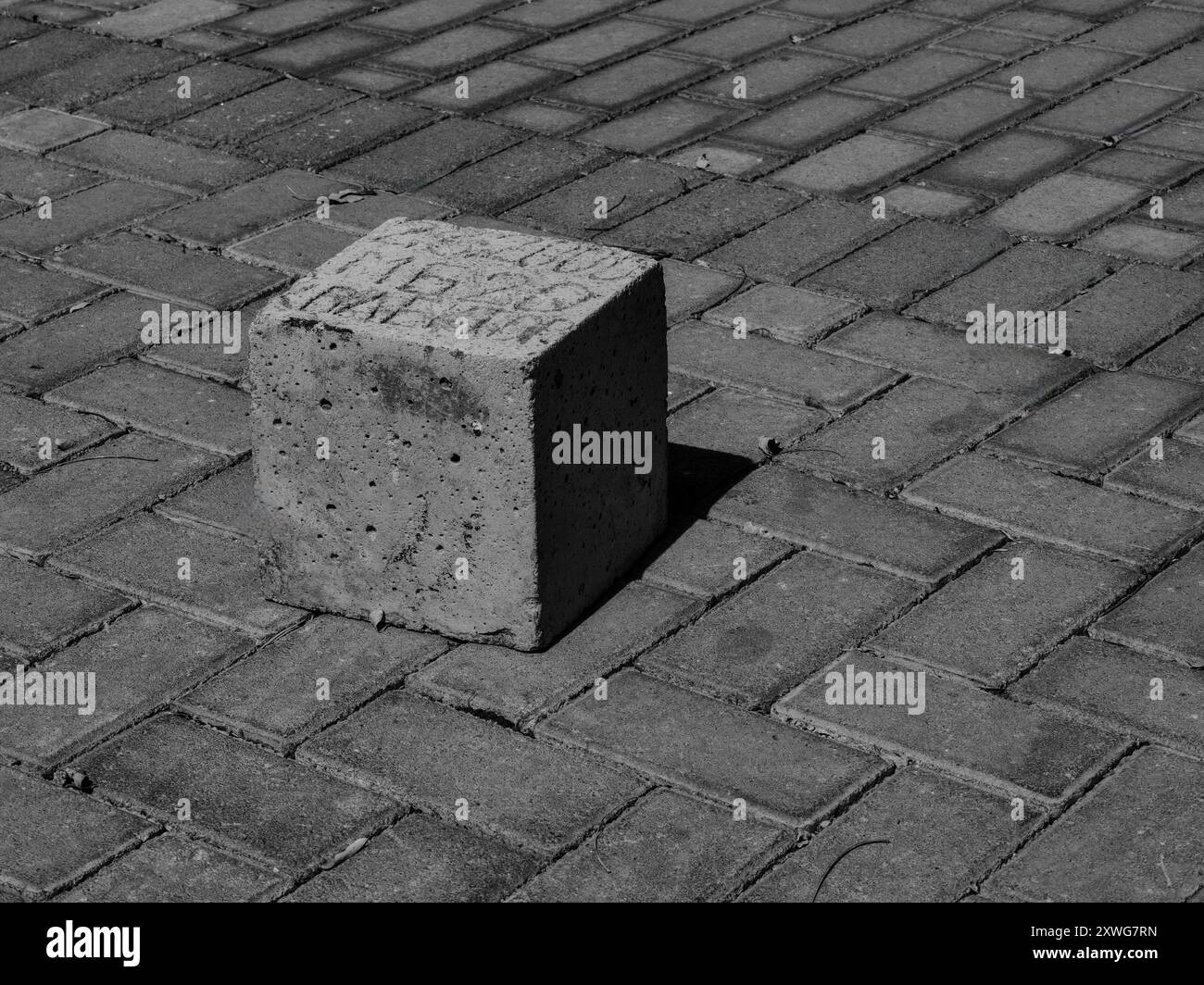 Quadratischer Stein auf dem Bürgersteig: Muster, Textur und das Spiel von Licht und Schatten – Burdens Konzept. Schwarzweiß. Stockfoto