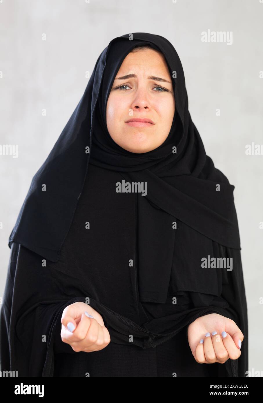 Die junge muslimische Frau in schwarzem Hijab ist über schlechte Nachrichten verärgert und hält ihre Hände dejektiv hoch. Stockfoto