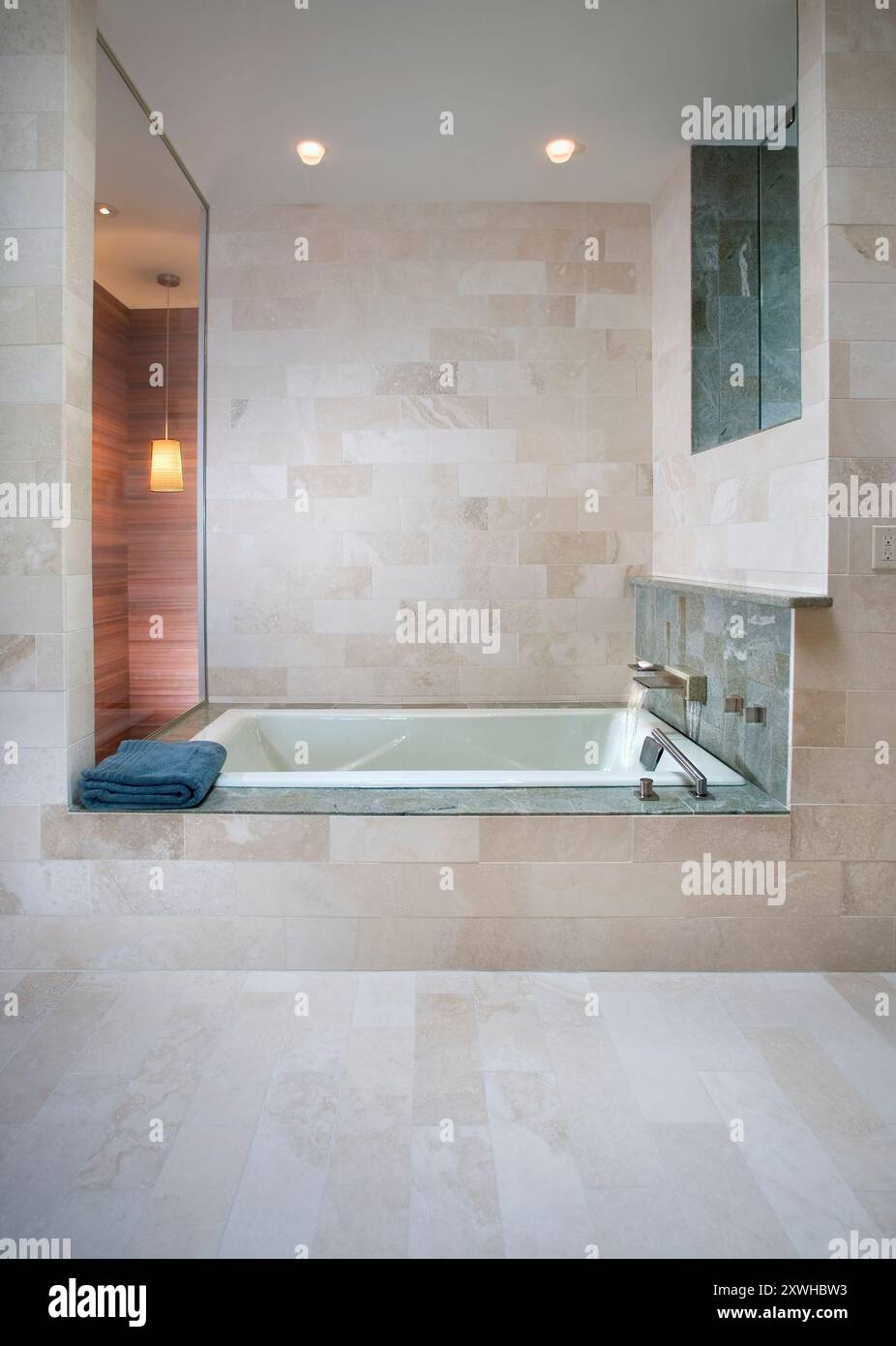 Moderne Badewanne mit cremefarbenen Steinfliesen und zwei Fenstern Stockfoto