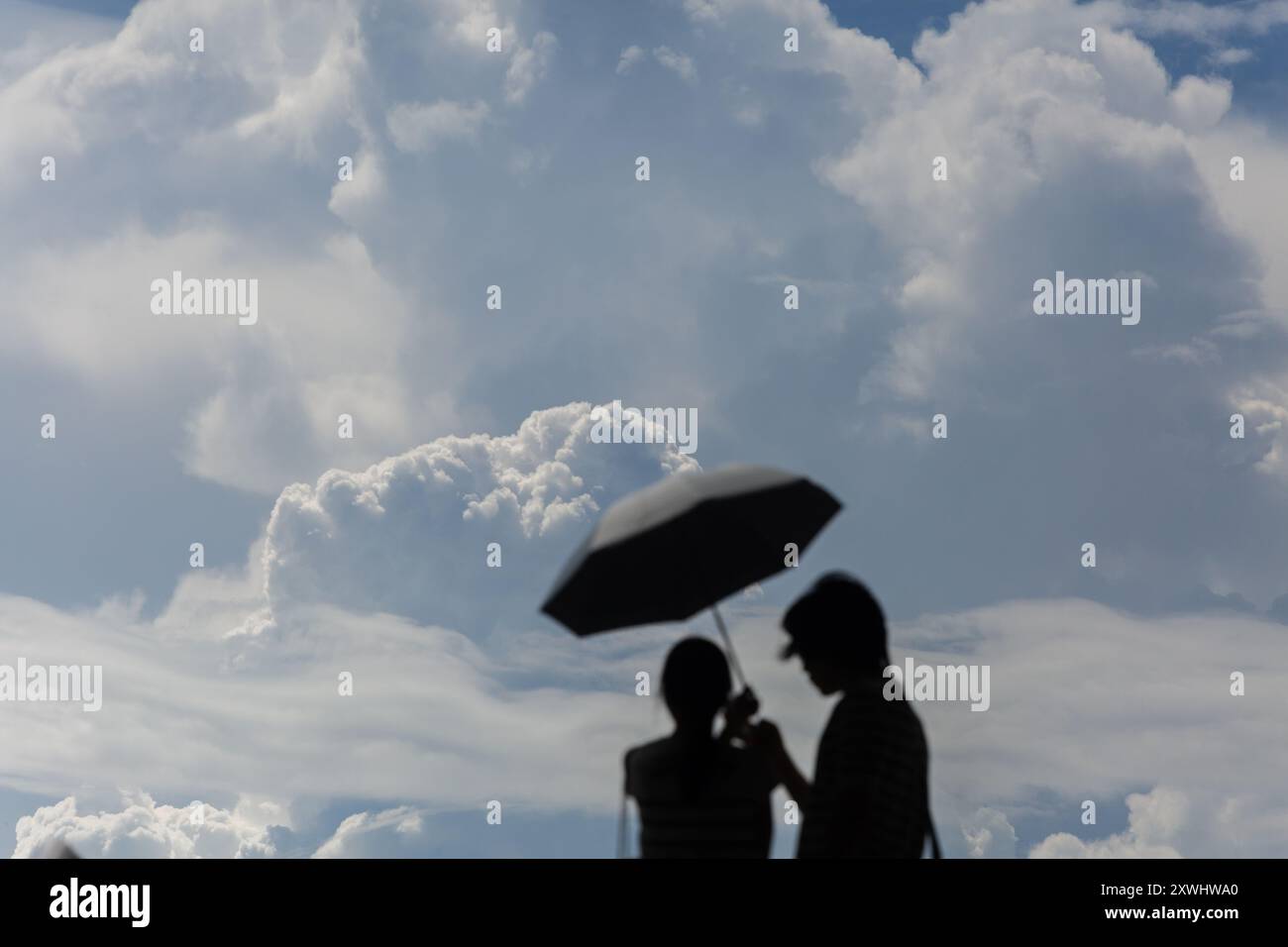 August 2024. Besucher, die sich mit einem Regenschirm vor der sonnigen Hitze, dem hohen UV-Wetter und den am Himmel sichtbaren Kumuluswolken schützen. Singapur. Stockfoto