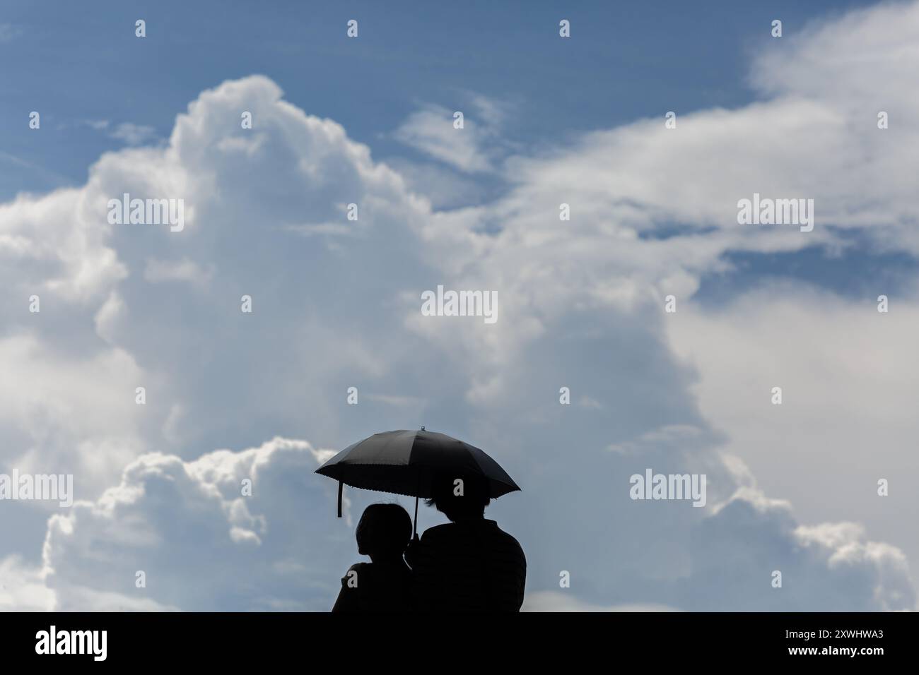 August 2024. Besucher, die sich mit einem Regenschirm vor der sonnigen Hitze, dem hohen UV-Wetter und den am Himmel sichtbaren Kumuluswolken schützen. Singapur. Stockfoto