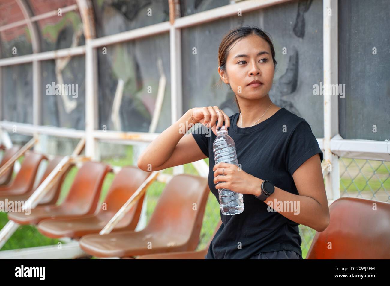 Junge asiatische Läuferin, die während ihrer Laufpause den Verschluss ihrer Trinkflasche öffnet Stockfoto