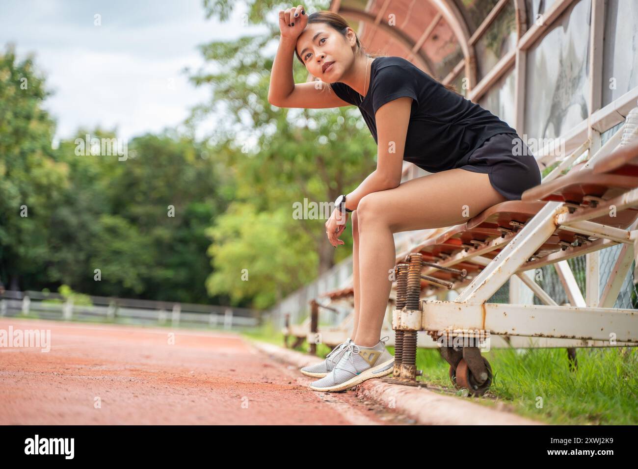 Müde Läuferin, die sich hinsetzt, um eine Pause von ihrem Lauf auf einer Outdoor-Laufstrecke zu machen Stockfoto