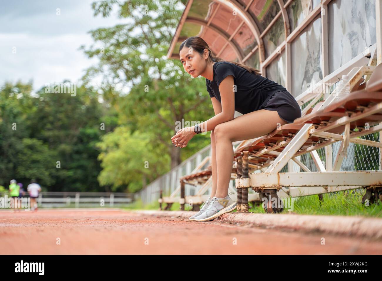 Müde Läuferin, die sich hinsetzt, um eine Pause von ihrem Lauf auf einer Outdoor-Laufstrecke zu machen Stockfoto