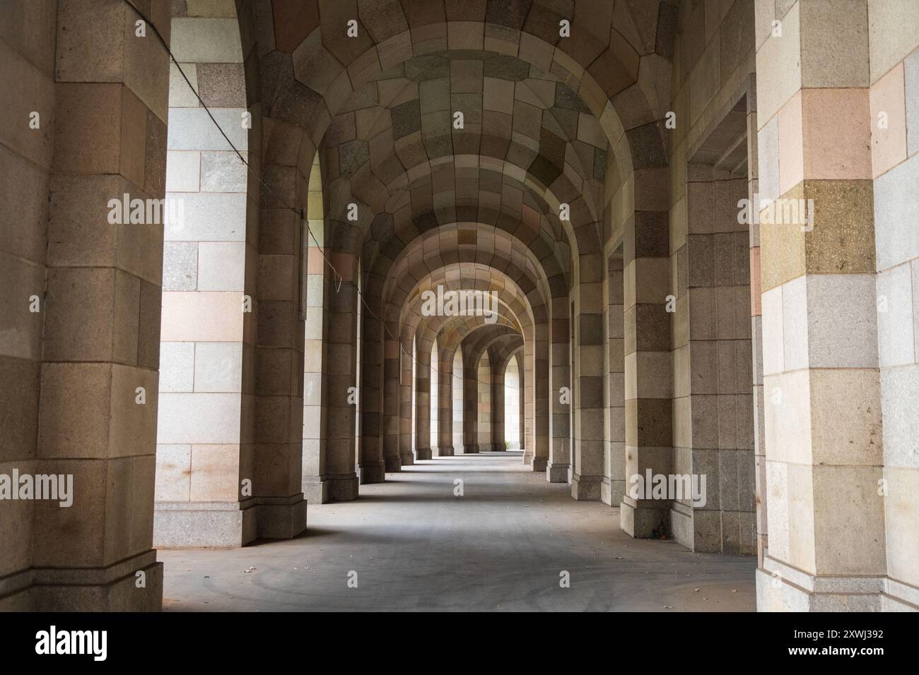 Eine Reihe hoher bogenförmiger Öffnungen bildet einen steinernen Säulengang innerhalb der Kongresshalle, durch die Licht fällt, Nürnberg, Bayern, Deutschland. Stockfoto