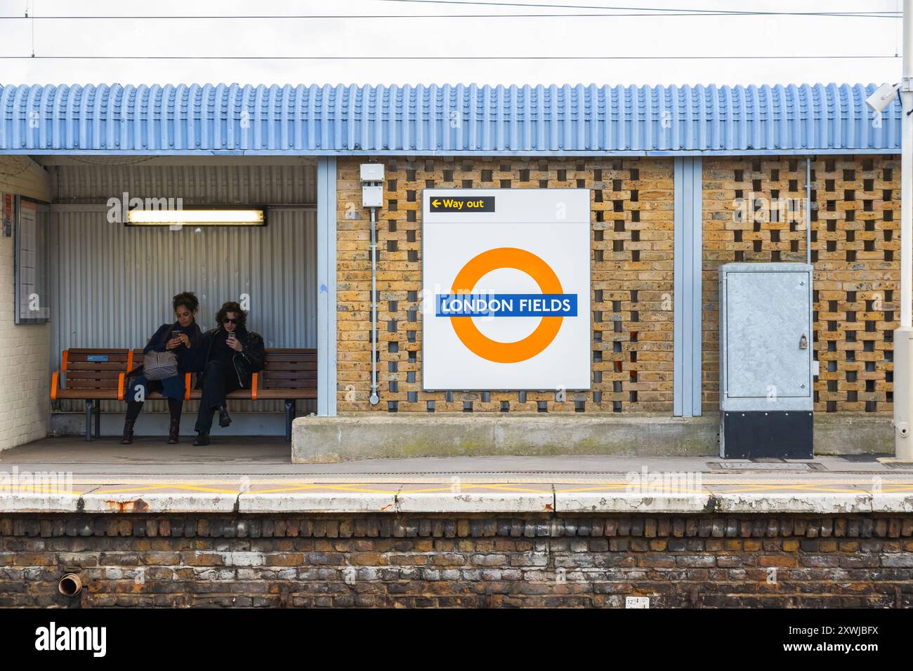 London, Großbritannien - 25. Januar 2024 - Passagiere, die auf der Bank sitzen und am Bahnsteig des Londoner Feldbahnhofs warten Stockfoto