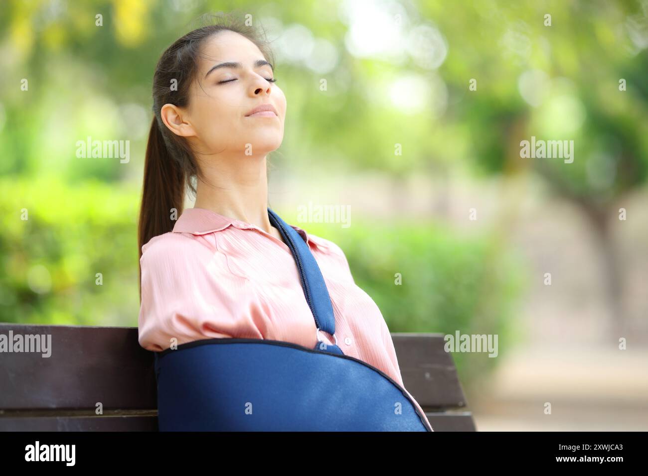 Rekonvaleszierende Frau mit gebrochenem Arm, die frische Luft in einem Park atmet Stockfoto