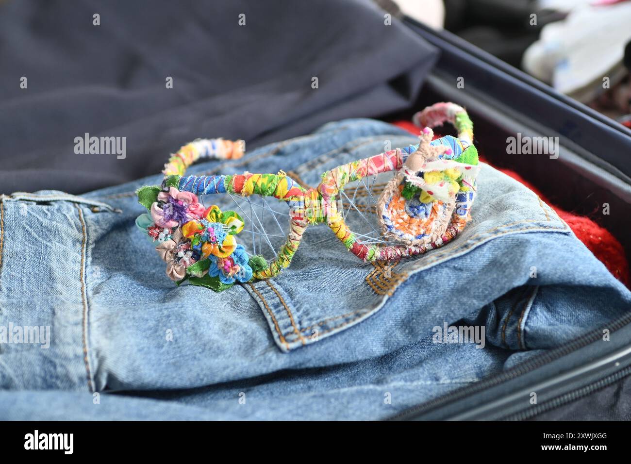 Eine einzigartige und farbenfrohe handgefertigte Brille aus Materialien liegt auf einer blauen Jeans. Die Brille ist ein kreativer und modischer Zugang Stockfoto