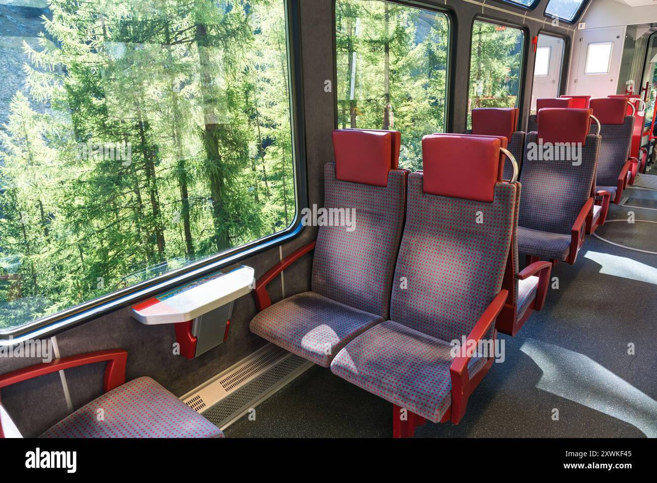 Im Inneren eines elektrischen Zuges mit rotem Sitz auf der Bahn, die das Tal in den Schweizer Alpen in der Schweiz durchquert Stockfoto