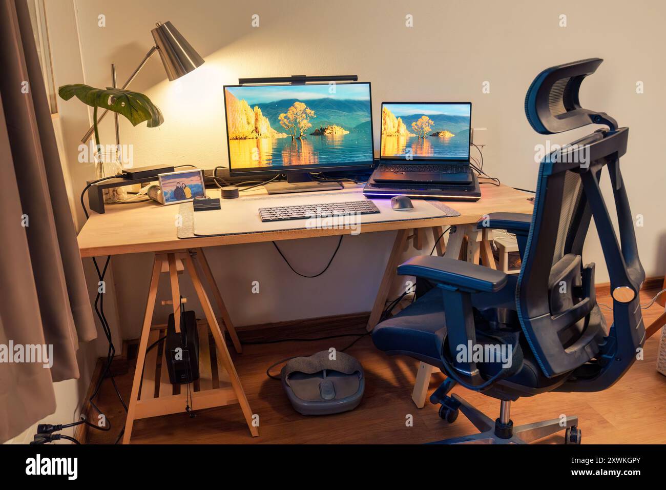 Innenarbeitsplatz des Fotografen mit Laptop, Monitor, Computergerät, Lichtlampe, grünem Blatt auf Holztisch und ergonomischem Stuhl im Haus Stockfoto