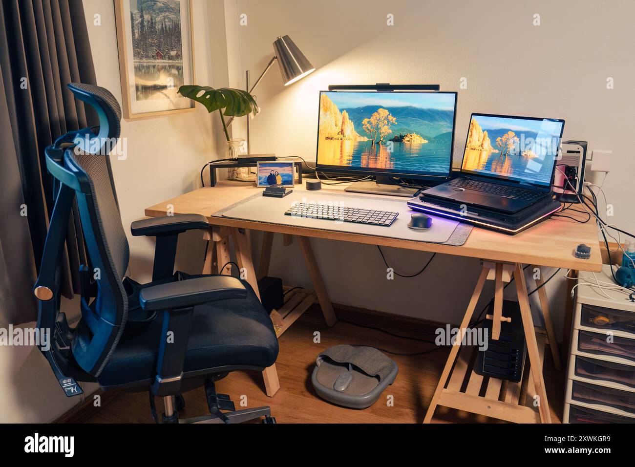 Innenarbeitsplatz des Fotografen mit Laptop, Monitor, Computergerät, Lichtlampe, grünem Blatt auf Holztisch und ergonomischem Stuhl im Haus Stockfoto
