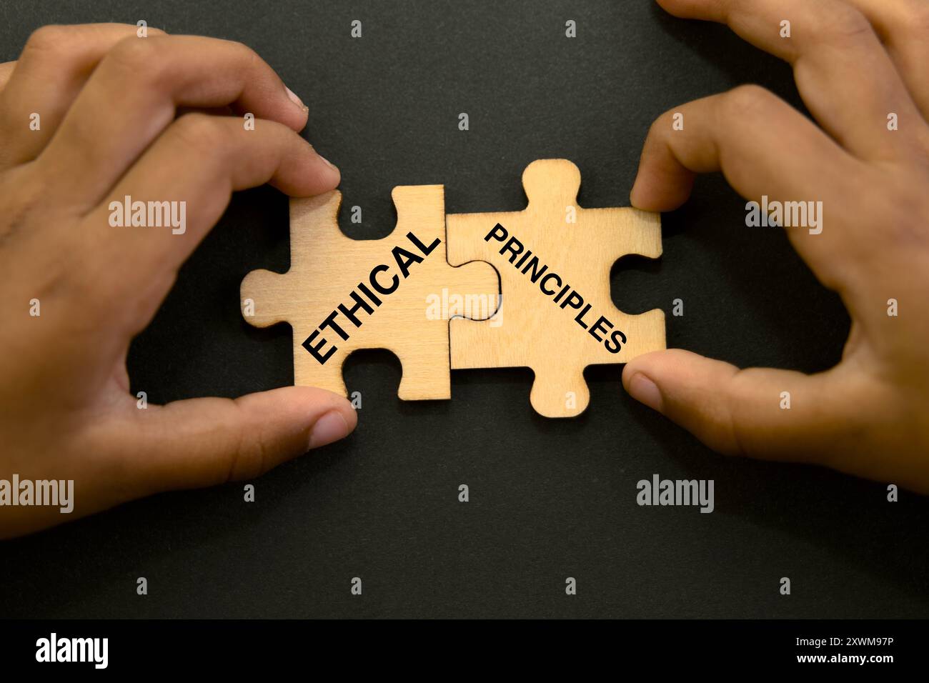 Zwei Hände verbinden Puzzleteile mit der Bezeichnung „ethisch“ und „Prinzipien“ und symbolisieren Integrität und moralische Entscheidungsfindung. Stockfoto