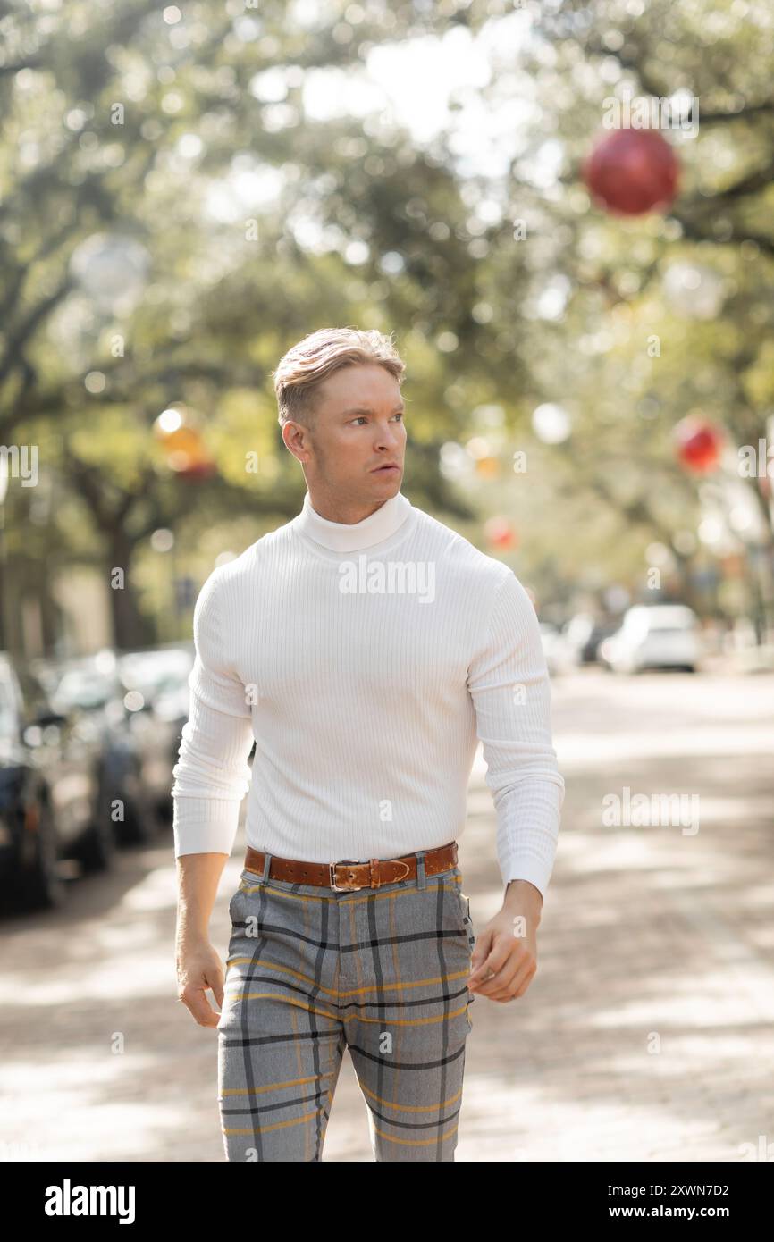 Ein gut aussehender blonder Mann in einem weißen Rollkragen und karierten Hosen läuft eine Florida Straße entlang. Stockfoto