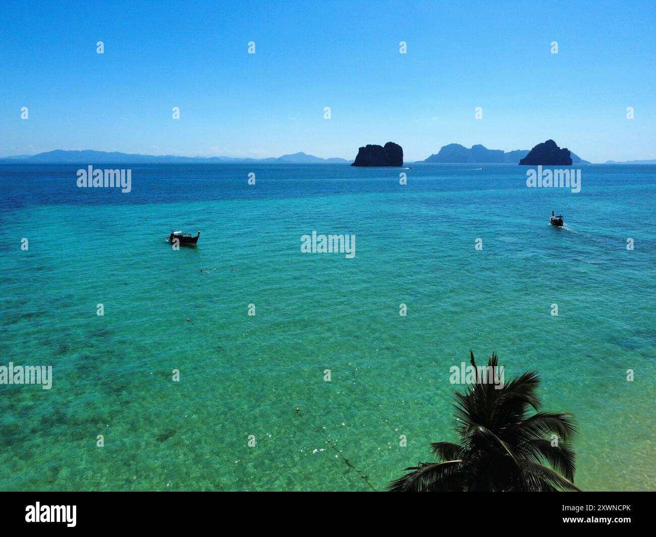 Aus der Vogelperspektive auf das Meer am Ko Ngai Paradise Beach an einem sonnigen Tag mit langen Booten, die über das türkisfarbene Wasser und Korallenriff segeln Stockfoto