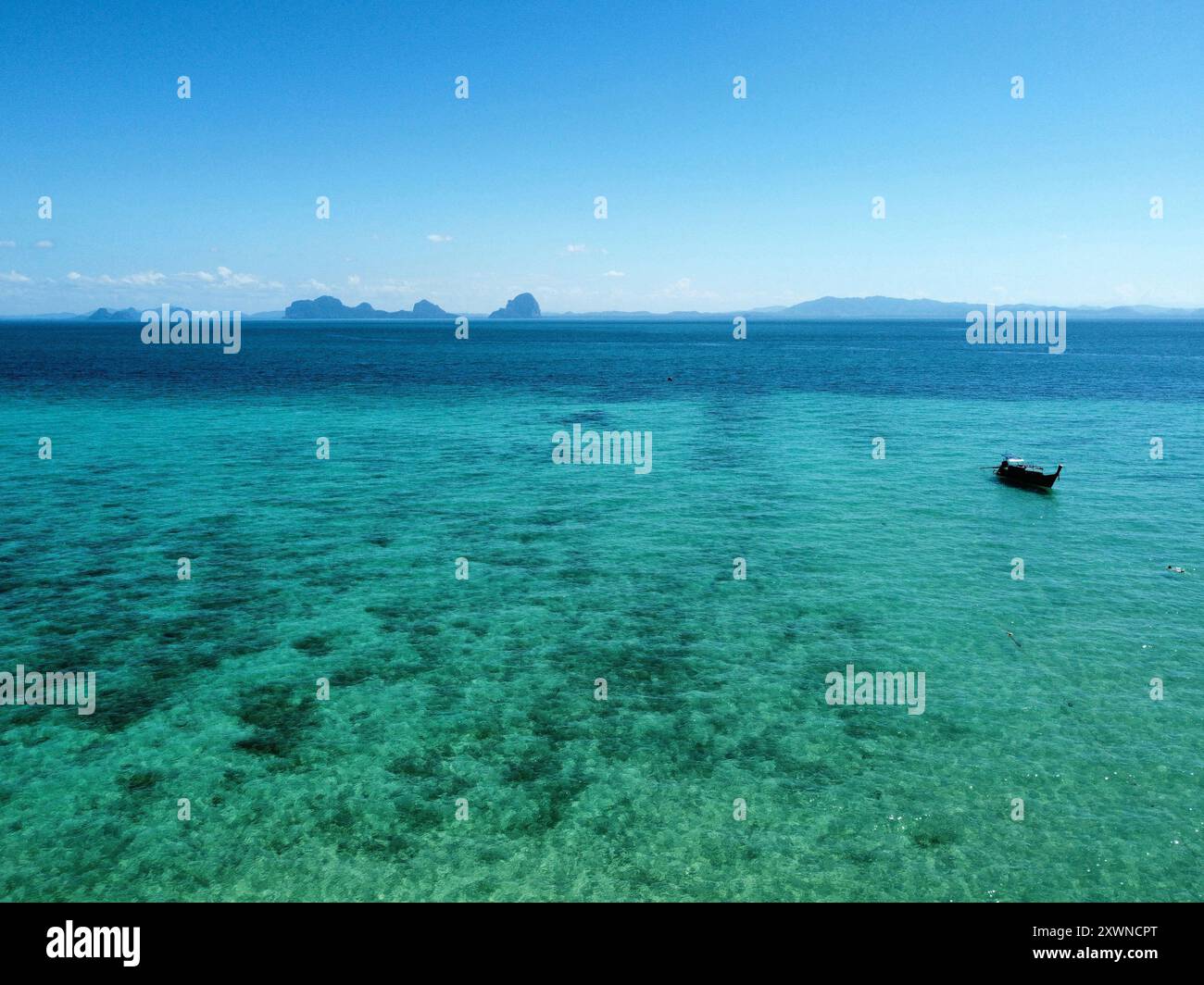 Aus der Vogelperspektive auf das Meer am Ko Ngai Paradise Beach an einem sonnigen Tag mit einem langen Boot, das über das türkisfarbene Wasser und Korallenriff segelt Stockfoto