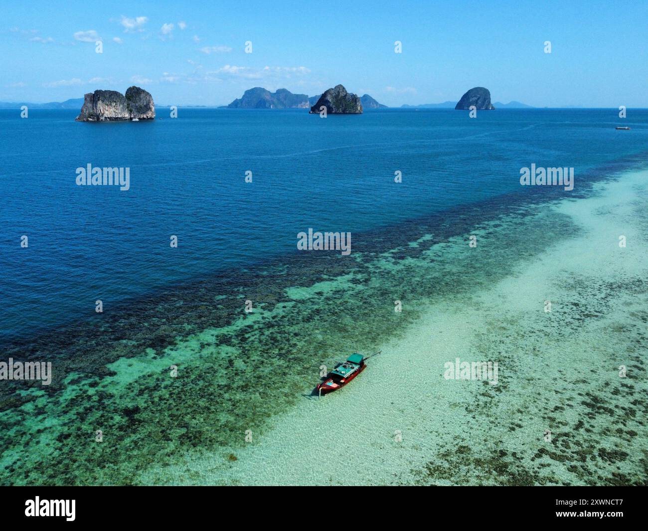 Luftbild der Küste von Ko Ngai mit einem langen Boot auf dem türkisfarbenen Wasser und Inseln im Hintergrund Stockfoto