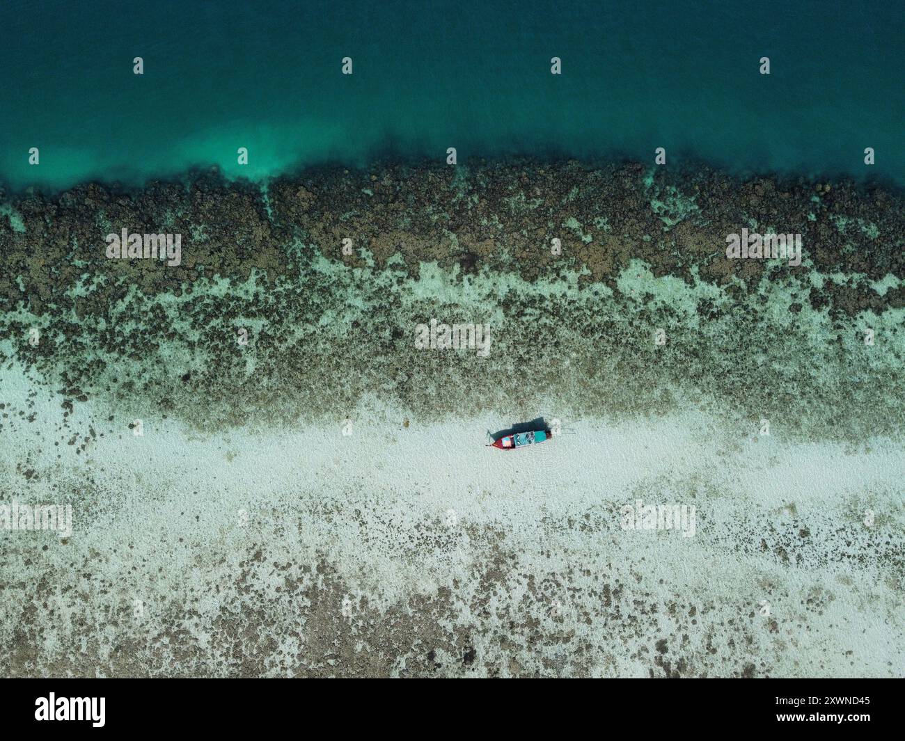 Aus der Vogelperspektive eines Langboot, das durch das türkisfarbene Wasser neben einer Unterwasserklippe segelt, die vom Korallenriff auf Ko Ngai in Trang, Thailand, gebildet wird Stockfoto