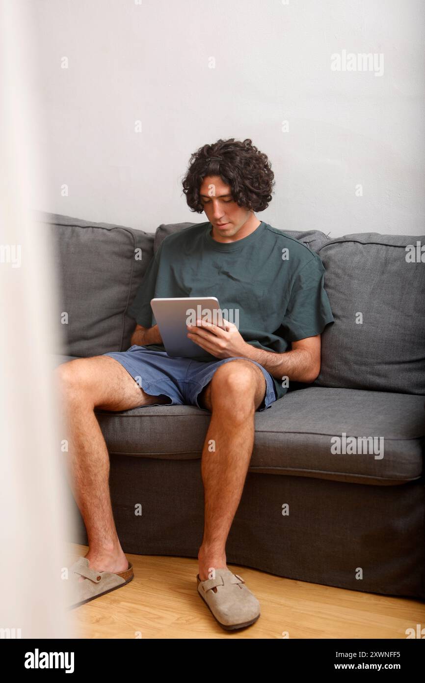 Junger Kerl mit Tablet auf dem Sofa zu Hause Stockfoto