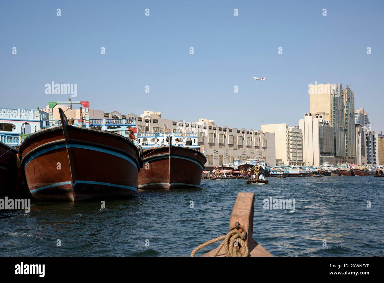 Dubai, VAE, 3. April 2015. Malerischer Blick auf den Dubai Creek von einem Abra aus, mit einem Wassertaxi-Pier und einem Emirates-Flugzeug am blauen Himmel Stockfoto