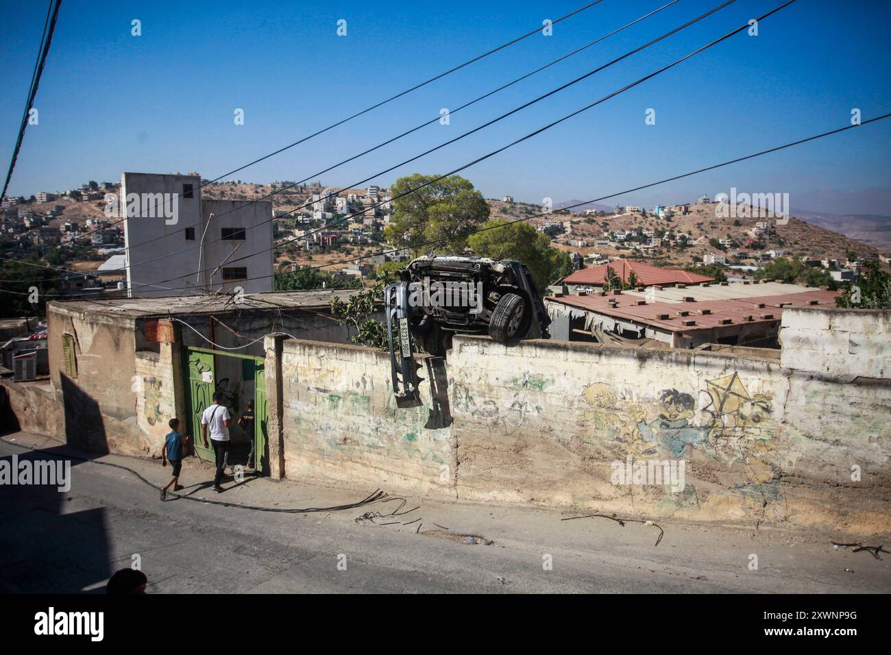 Tubas, Palästina. August 2024. Palästinenser sahen, wie sie ein Tor in der Nähe eines beschädigten Autos betreten, das von israelischen Truppen während eines Überfalls demamiert wurde. Israelische Truppen überfielen ein Haus in der Stadt Tamoun, zerstörten es und verbrannten es und verhafteten vier junge Männer, die sich darin befanden. Quelle: SOPA Images Limited/Alamy Live News Stockfoto