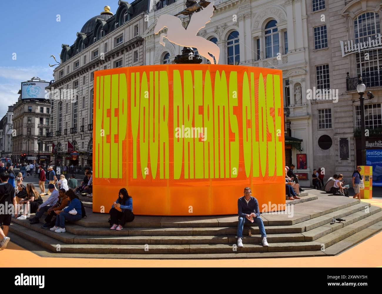 London, Großbritannien. August 2024. Neben der neuen Kunstinstallation „Good Things Come That Who Wait“ von Yinka Ilori sitzt man am Shaftesbury Memorial Fountain, im Volksmund Eros, im Piccadilly Circus. Quelle: SOPA Images Limited/Alamy Live News Stockfoto