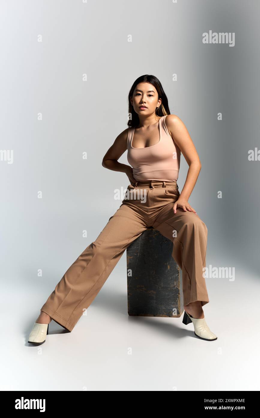 Eine asiatische Frau in einem hellrosa Oberteil und einer braunen Hose posiert auf einem Betonblock. Stockfoto
