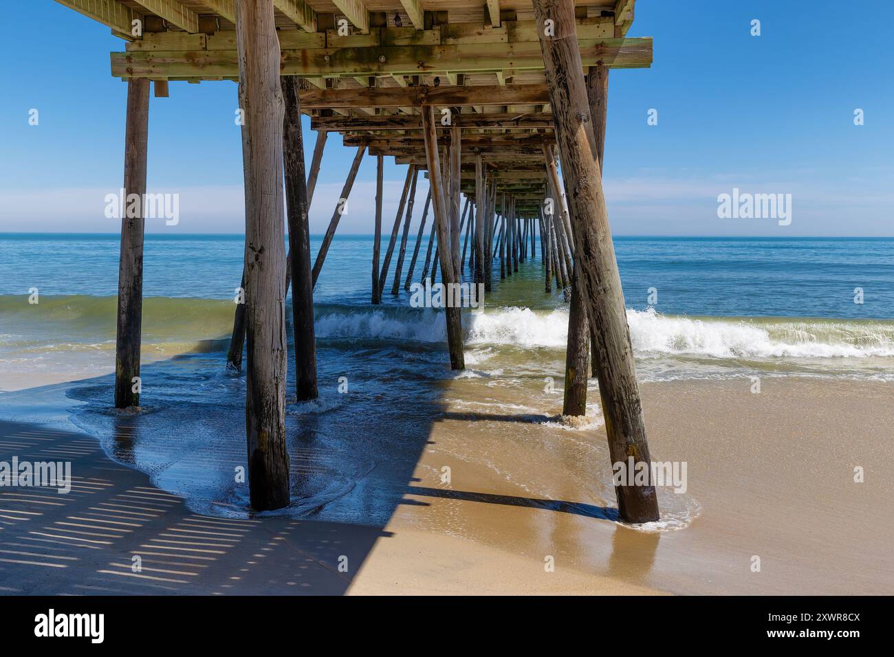 Avon Fishing Pier vier von unten vom Strand, während kleine Wellen vom Atlantischen Ozean hereinRollen. Stockfoto