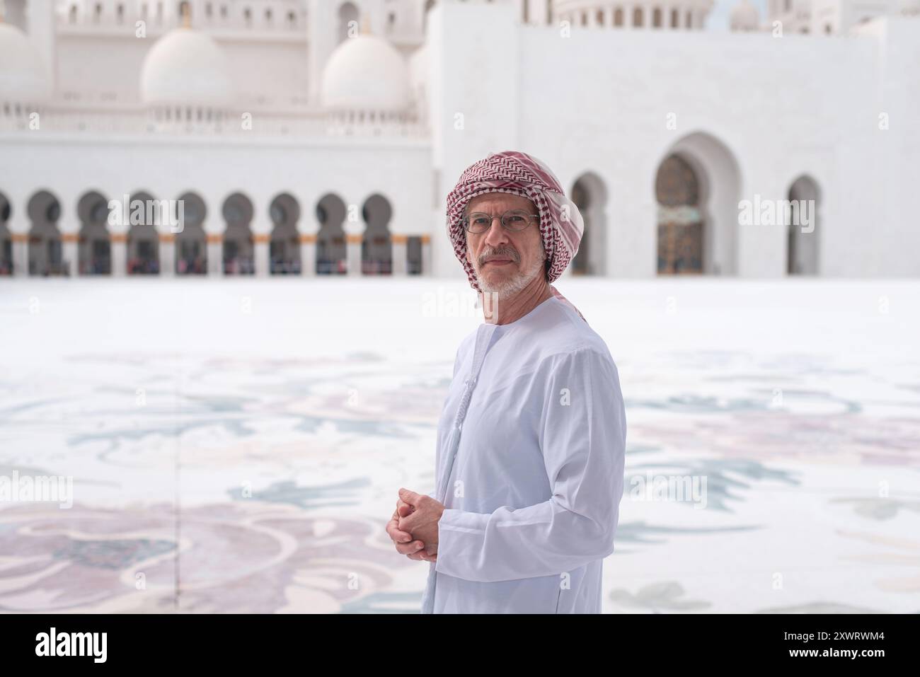 Ein Mann in Kanroa-traditioneller arabischer Kleidung steht vor der Scheich-Zayed-Moschee in Abu Dhabi mit majestätischen Kuppeln und Bögen im Hintergrund, cr Stockfoto