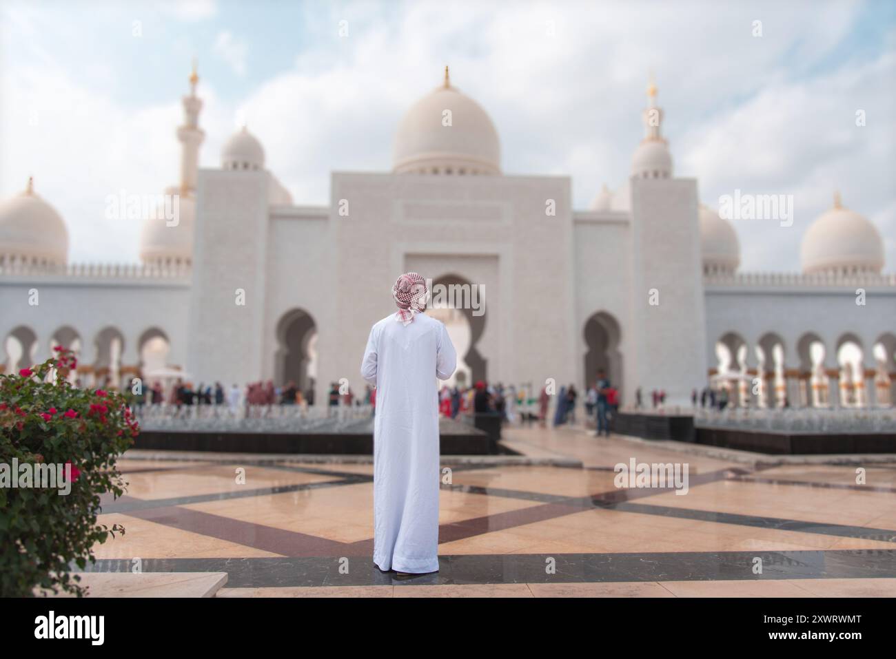Arabischer Mann in Kandora, der die beeindruckende Architektur der Scheich-Zayed-Moschee in Abu Dhabi mit prominenten Kuppeln und detaillierten Designs bewundert, Stockfoto