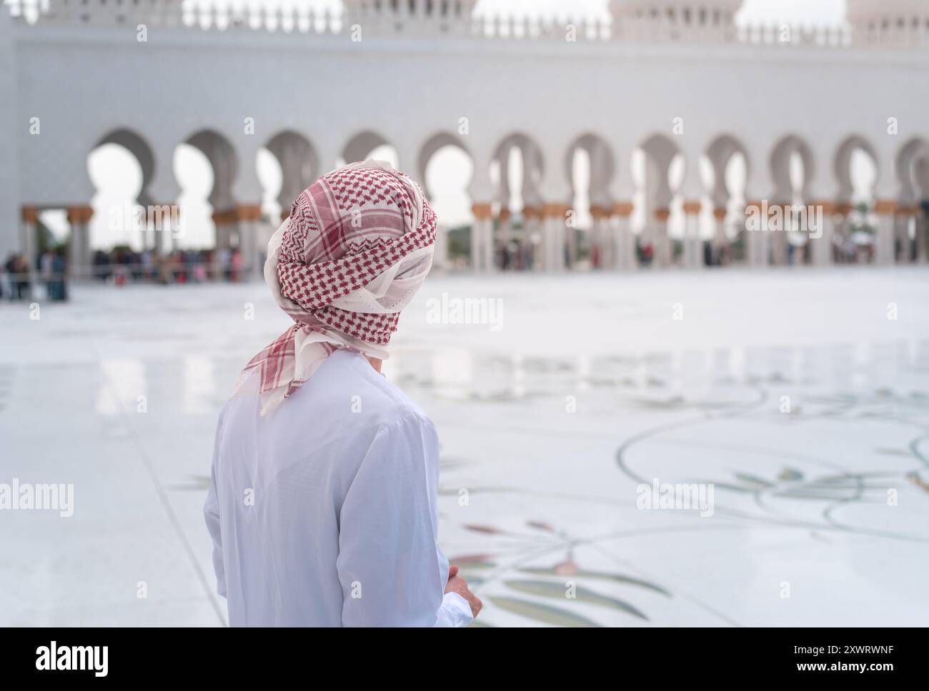 Arabischer Mann in Kandora steht in der Scheich-Zayed-Moschee im Innenhof von Abu Dhabi und zeigt eindrucksvolle islamische Architektur mit komplizierter Kuppel de Stockfoto